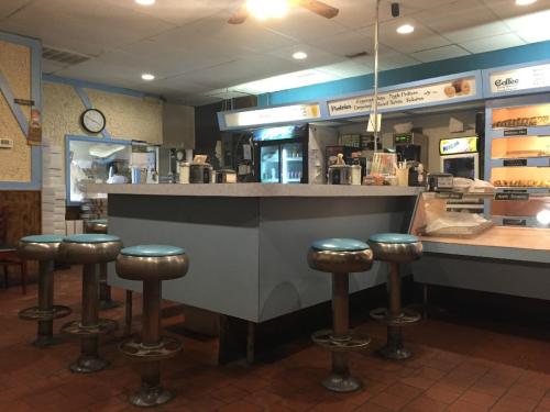 A cozy diner interior featuring a blue counter, metal stools, and a coffee station, with a clock on the wall.