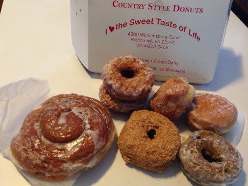 A variety of donuts, including glazed and crumb-coated, arranged on a table next to a donut box.