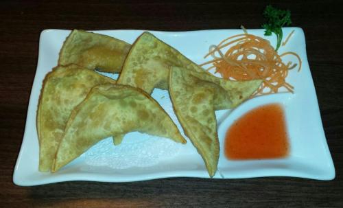 A plate of golden-brown samosas served with a side of sweet chili sauce and garnished with shredded carrots.
