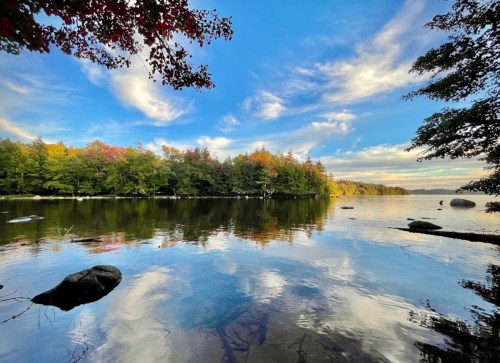 A serene lake scene with colorful trees reflecting in the water under a blue sky with fluffy clouds.