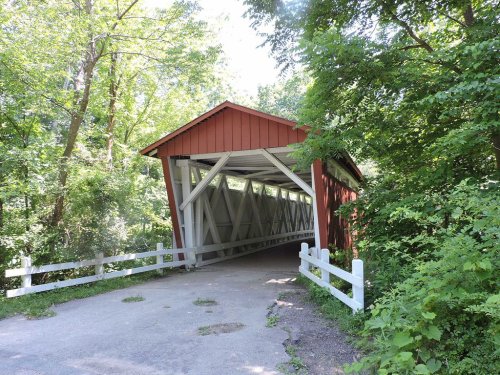 A red covered bridge surrounded by lush green trees and a gravel path leading to it.