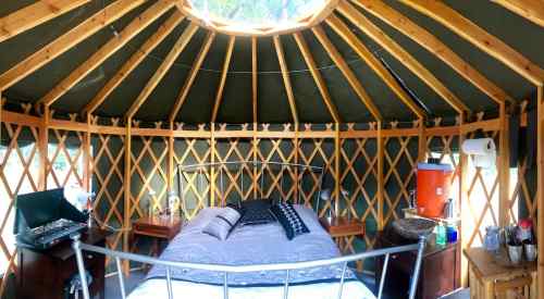 Interior of a yurt featuring a bed, wooden lattice walls, and a skylight, creating a cozy, rustic atmosphere.