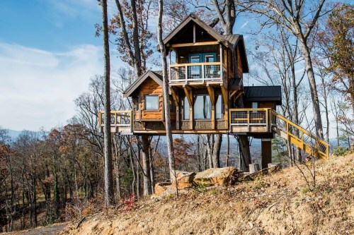 A wooden treehouse perched among trees, featuring balconies and a scenic view of the surrounding landscape.