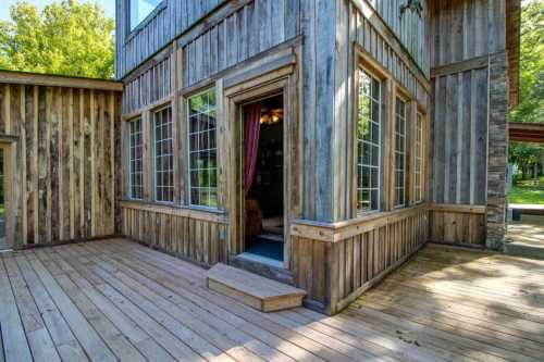 A wooden exterior of a house with large windows and a small step leading to an entrance, surrounded by greenery.