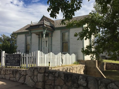 Historic white house with green trim, marked as the Dalton Gang Hideout, surrounded by a stone wall and picket fence.