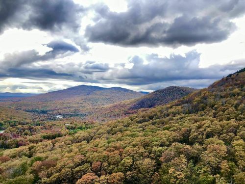 A panoramic view of rolling hills covered in autumn foliage under a cloudy sky.