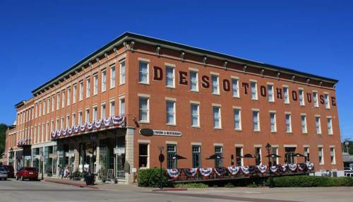 Historic DeSoto House Hotel with red brick exterior, flags, and awnings, set against a clear blue sky.