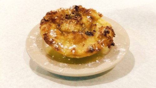 A golden-brown baked dessert on a small plate, dusted with powdered sugar and featuring a fluffy, textured surface.