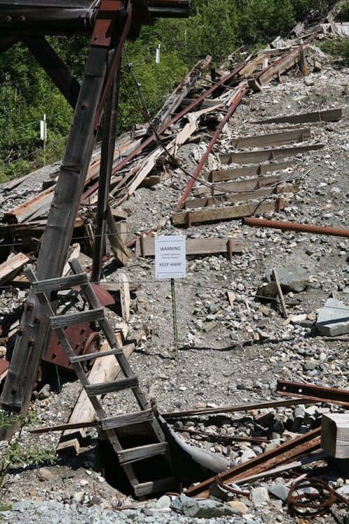 A weathered wooden structure with stairs leads to a rocky area, marked by a warning sign to keep away.