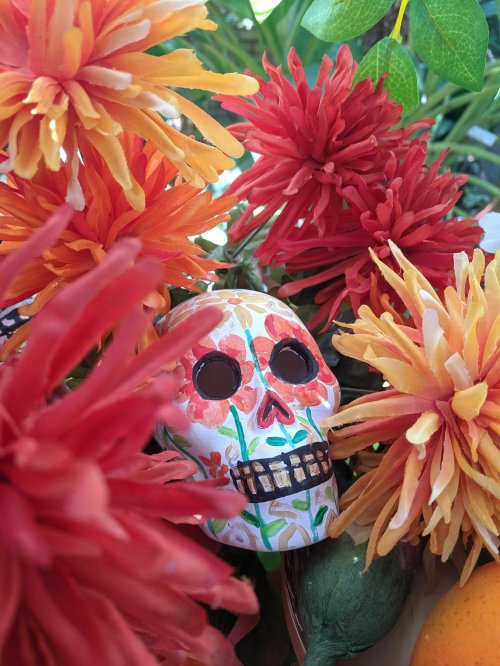 A colorful decorative skull surrounded by vibrant orange and red flowers.