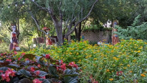 Colorful garden filled with yellow flowers, featuring decorative skeleton figures among lush greenery and trees.