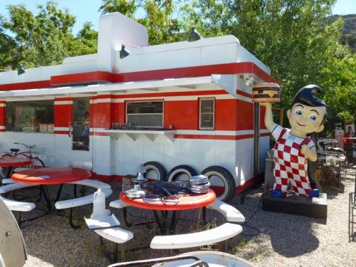 A retro diner with red and white decor, featuring a large cartoon chef statue and outdoor seating.