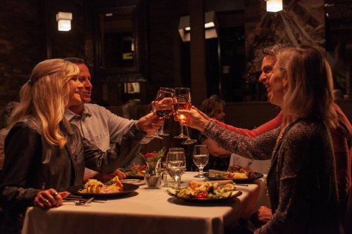 A group of four friends toasting with glasses of wine at a cozy restaurant table, enjoying dinner together.