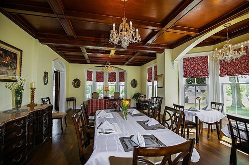 Elegant dining room with a wooden ceiling, chandeliers, and a table set for a meal, featuring floral centerpieces.