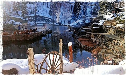 A serene winter scene featuring a snowy landscape, a calm pond, and rustic wooden structures.