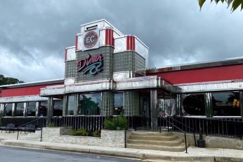 A retro-style diner with a shiny metal exterior and neon signage, set against a cloudy sky.