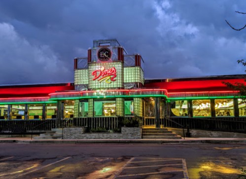A retro diner illuminated at night, featuring neon lights and a classic design against a cloudy sky.