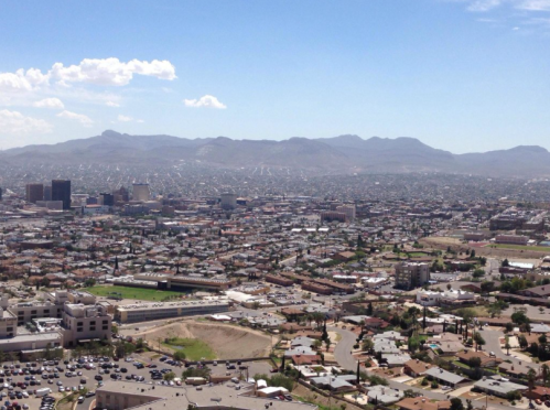 A panoramic view of a city with mountains in the background, featuring a mix of buildings and open land.