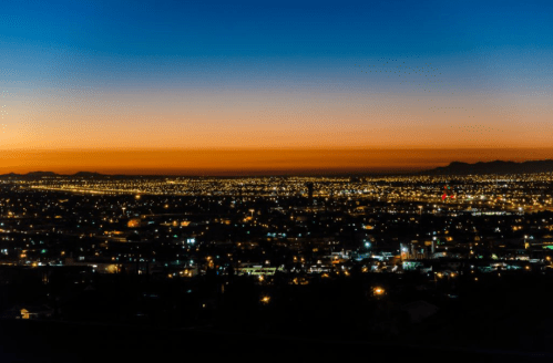 A panoramic view of a city skyline at dusk, with twinkling lights and a gradient sky transitioning from orange to blue.