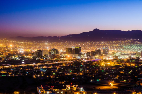 A panoramic view of a city skyline at dusk, with twinkling lights and mountains in the background.