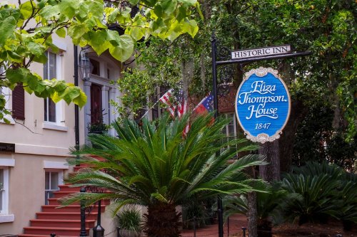 Sign for Eliza Thompson House, a historic inn, surrounded by greenery and flags in a charming setting.