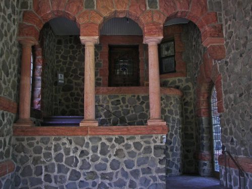 Interior view of a stone building featuring arched columns and a staircase, with textured walls and a rustic ambiance.
