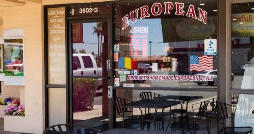 A storefront labeled "European" with outdoor seating, featuring an open sign and a display of flowers nearby.