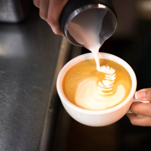 A barista pours steamed milk into a cup of coffee, creating a beautiful latte art design.