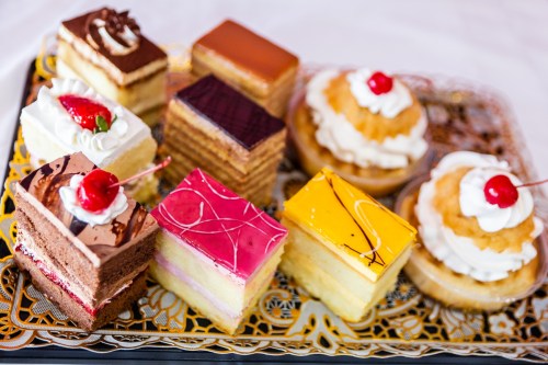 A colorful assortment of desserts, including layered cakes and pastries, topped with cherries and whipped cream.