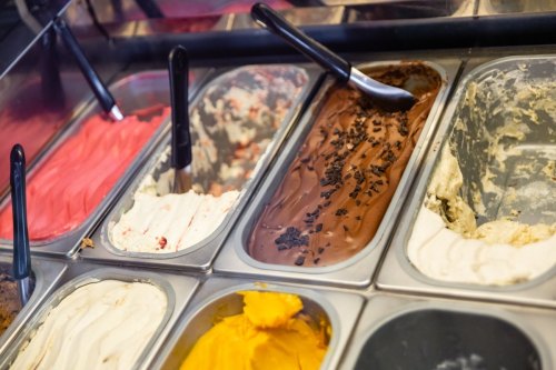 A variety of gelato flavors in metal containers, including chocolate, vanilla, and fruit options, with scoops.