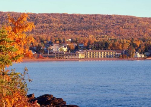 A scenic view of a lakeside hotel surrounded by autumn foliage and mountains in the background.