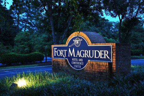 Sign for Fort Magruder Hotel and Conference Center, illuminated at dusk, surrounded by greenery.