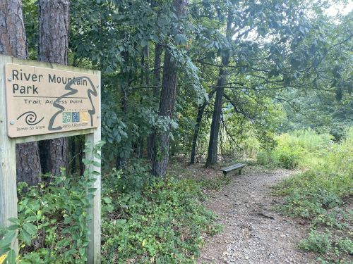 Sign for River Mountain Park trail access point, surrounded by trees and a gravel path leading into the woods.