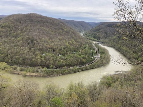 A scenic view of a winding river surrounded by lush green hills under a cloudy sky.