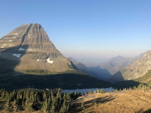 A scenic mountain landscape with a prominent peak, lush greenery, and a tranquil lake under a clear blue sky.