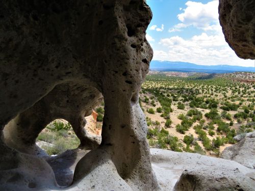 View through a rock formation, showcasing a vast landscape of greenery and distant mountains under a partly cloudy sky.