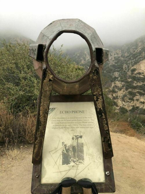 A metal echo phone sign at a scenic overlook, surrounded by foggy mountains and greenery.
