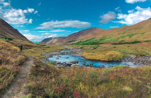 A scenic landscape featuring a winding river, colorful foliage, and mountains under a blue sky with scattered clouds.