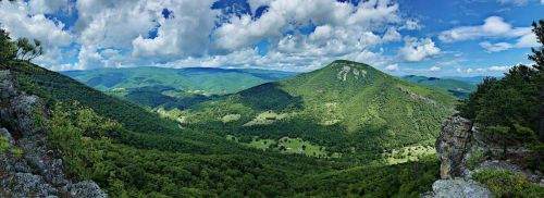 A panoramic view of lush green mountains and valleys under a bright blue sky with fluffy white clouds.