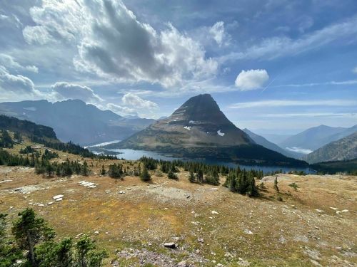 A scenic view of a mountain surrounded by a lake and lush greenery under a partly cloudy sky.