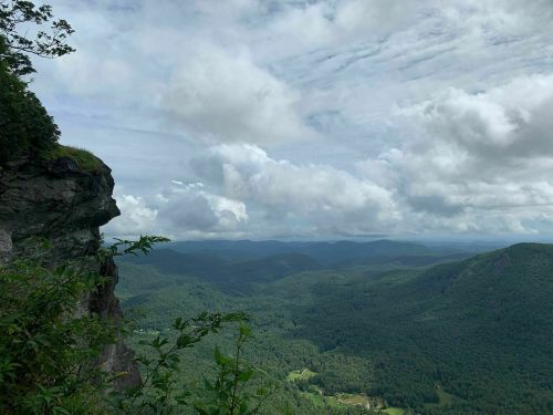 A scenic view from a rocky cliff overlooking lush green mountains and a cloudy sky.