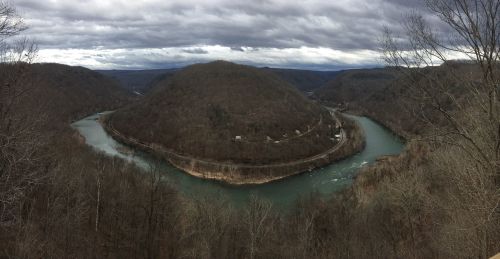 A panoramic view of a winding river surrounded by hills and overcast skies.