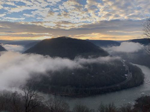 A scenic view of a river winding through mountains, with clouds and a colorful sunset in the background.