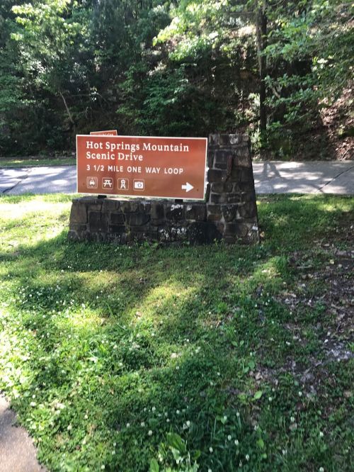 Sign for Hot Springs Mountain Scenic Drive, indicating a 3.5-mile one-way loop, surrounded by greenery.
