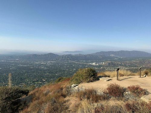 A panoramic view of a valley surrounded by mountains, with clear skies and sparse vegetation in the foreground.