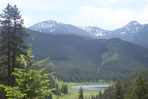 A scenic view of mountains with snow-capped peaks, surrounded by lush green forests and a serene lake below.