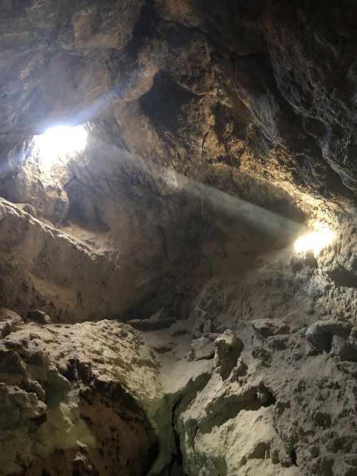 Light streams through openings in a rocky cave, illuminating the textured walls and creating a dramatic atmosphere.