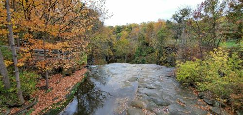 A serene waterfall surrounded by vibrant autumn foliage and rocky terrain, reflecting the colors of fall.
