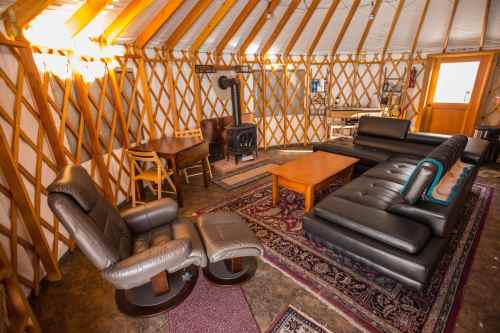 Cozy yurt interior featuring a seating area, wooden table, stove, and warm lighting.