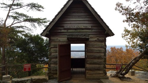 A rustic wooden cabin labeled "Meditation Point" with an open door, surrounded by trees and scenic views.